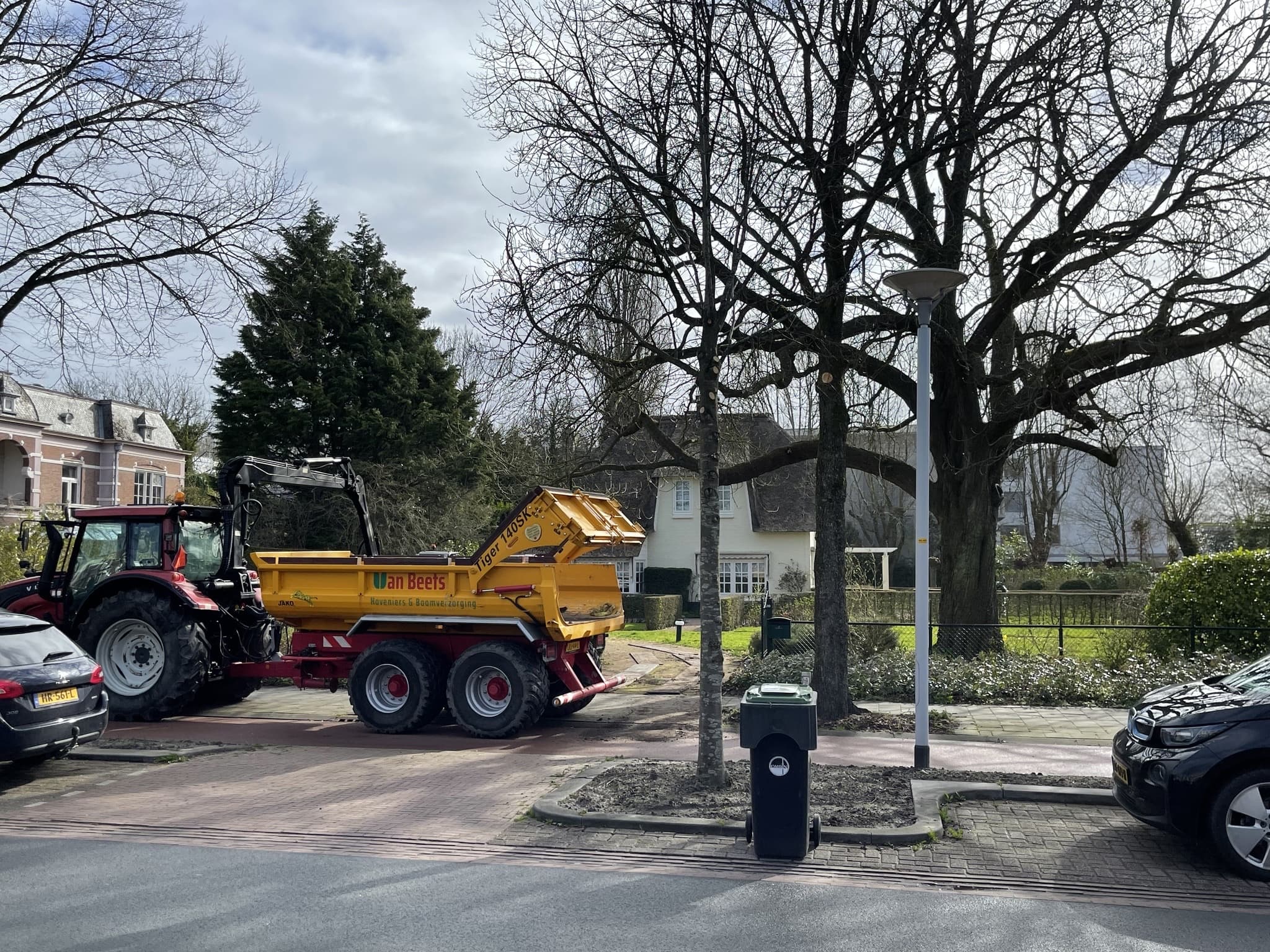 Gele kipper van Van Beets achter een trekker in een woonstraat, klaar om zand en grond te leveren