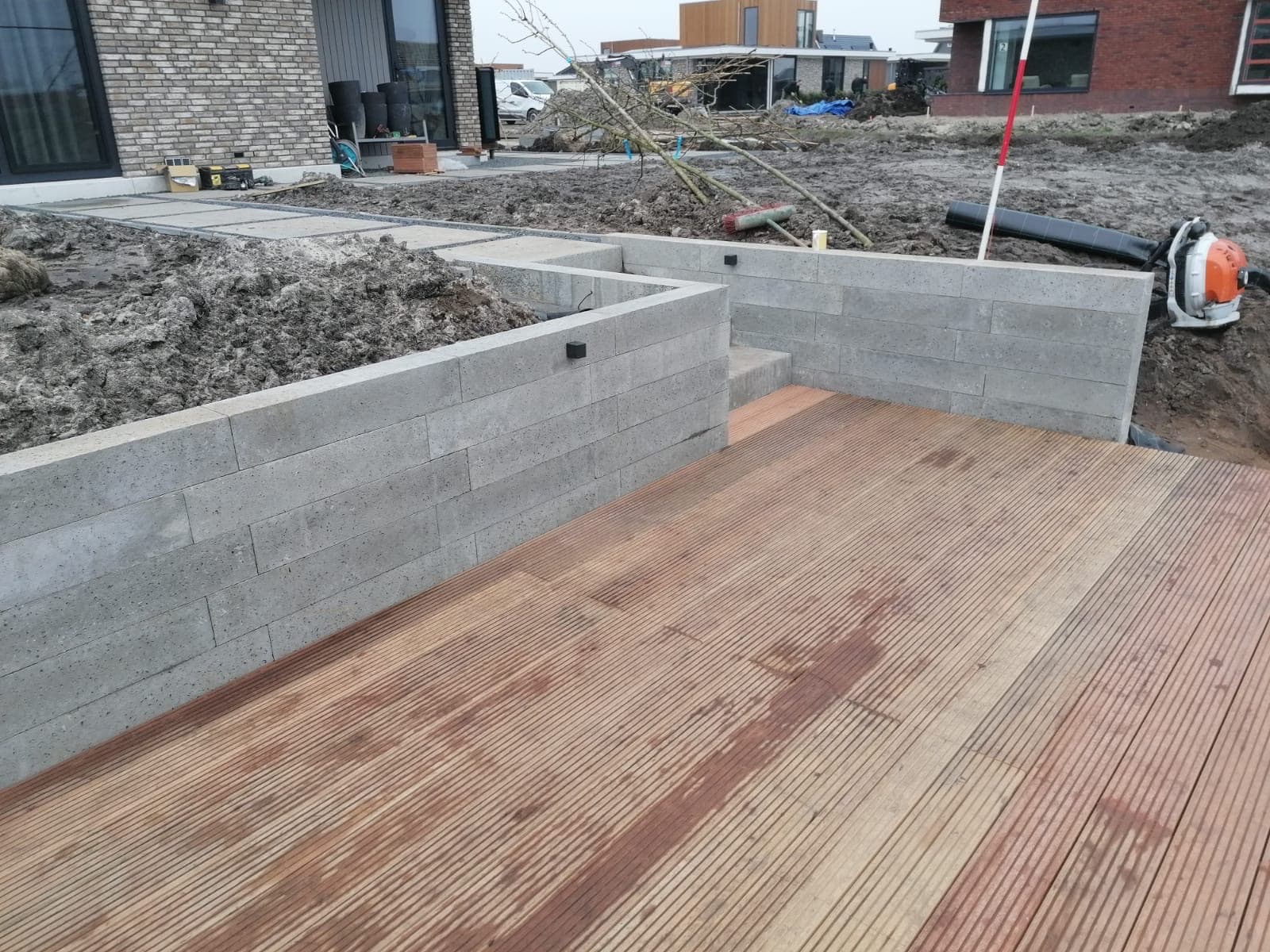 Betonnen keerwand met trede naast een houten vlonder bij een nieuwbouwwoning in aanleg