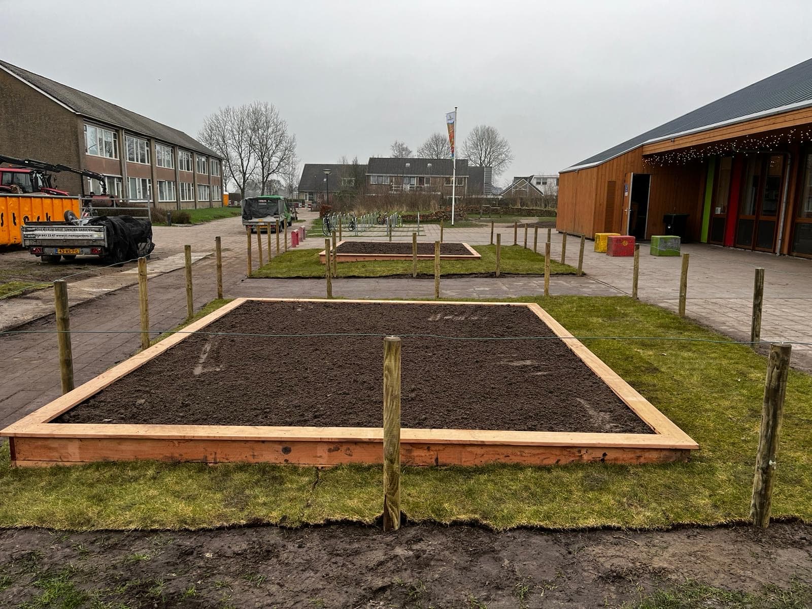Nieuw aangelegde moestuinbak met verse grond op een schoolplein, omringd door palen en gras
