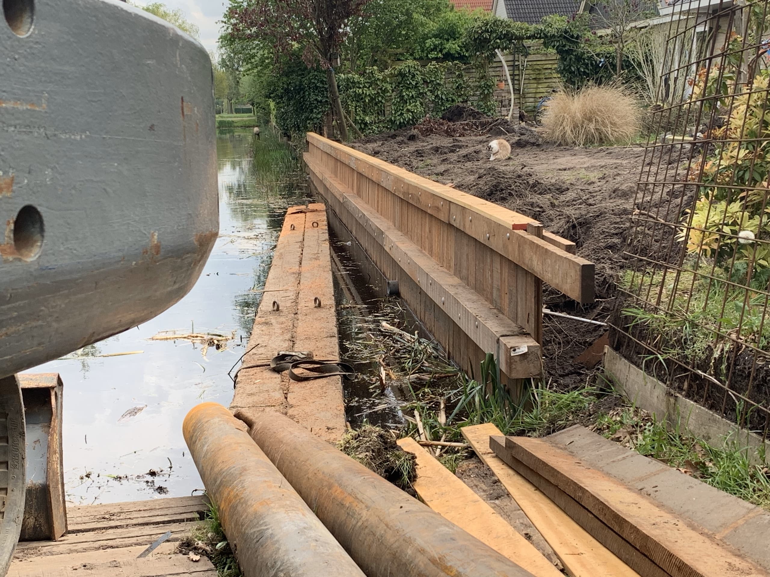 Stalen buizen en steigerplanken van de tijdelijke werkbrug liggen klaar naast de net geplaatste houten beschoeiing