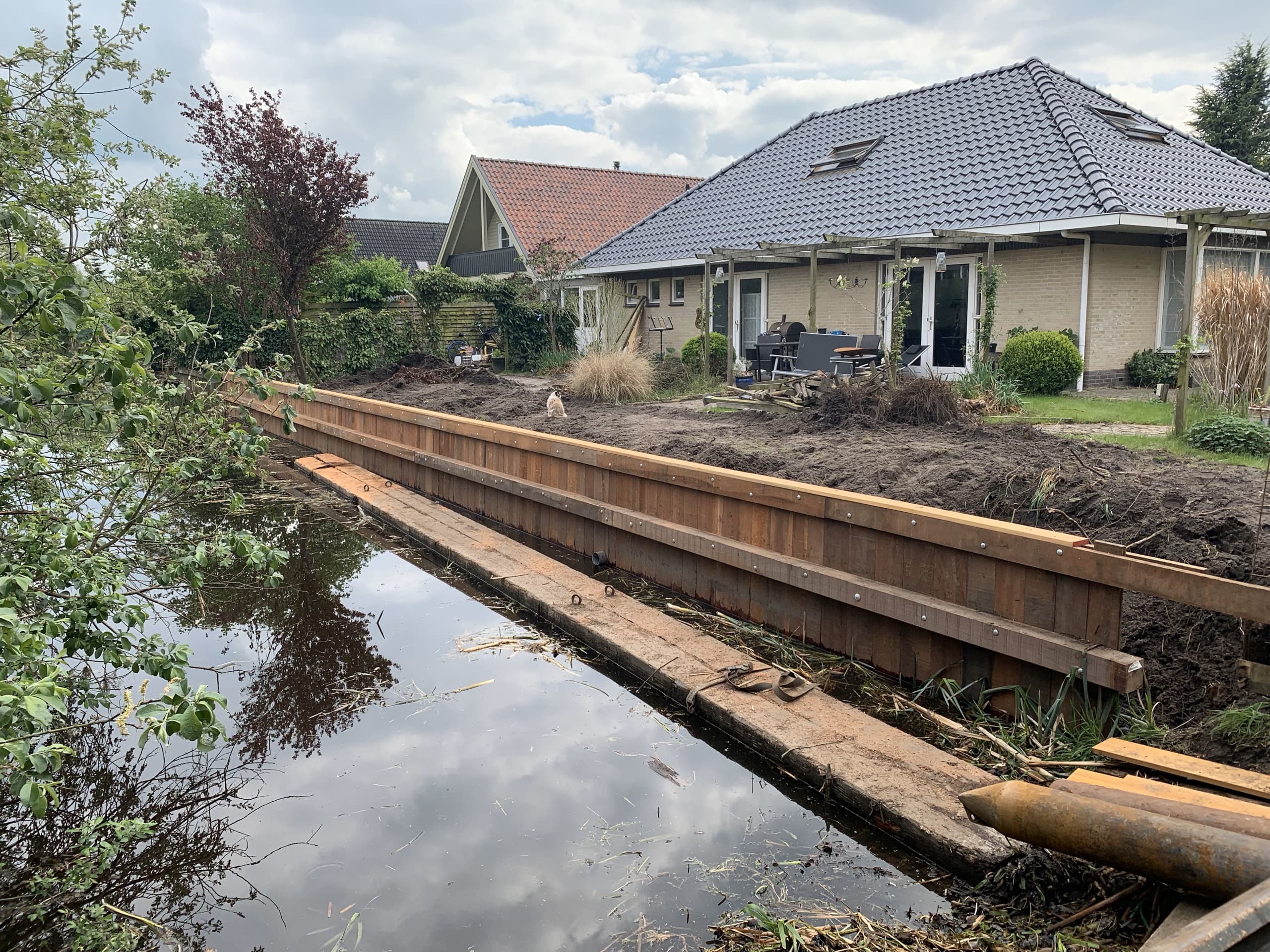 De nieuwe walbeschoeiing loopt over de volle breedte van de tuin, met de opgeworpen grond nog onafgewerkt erachter