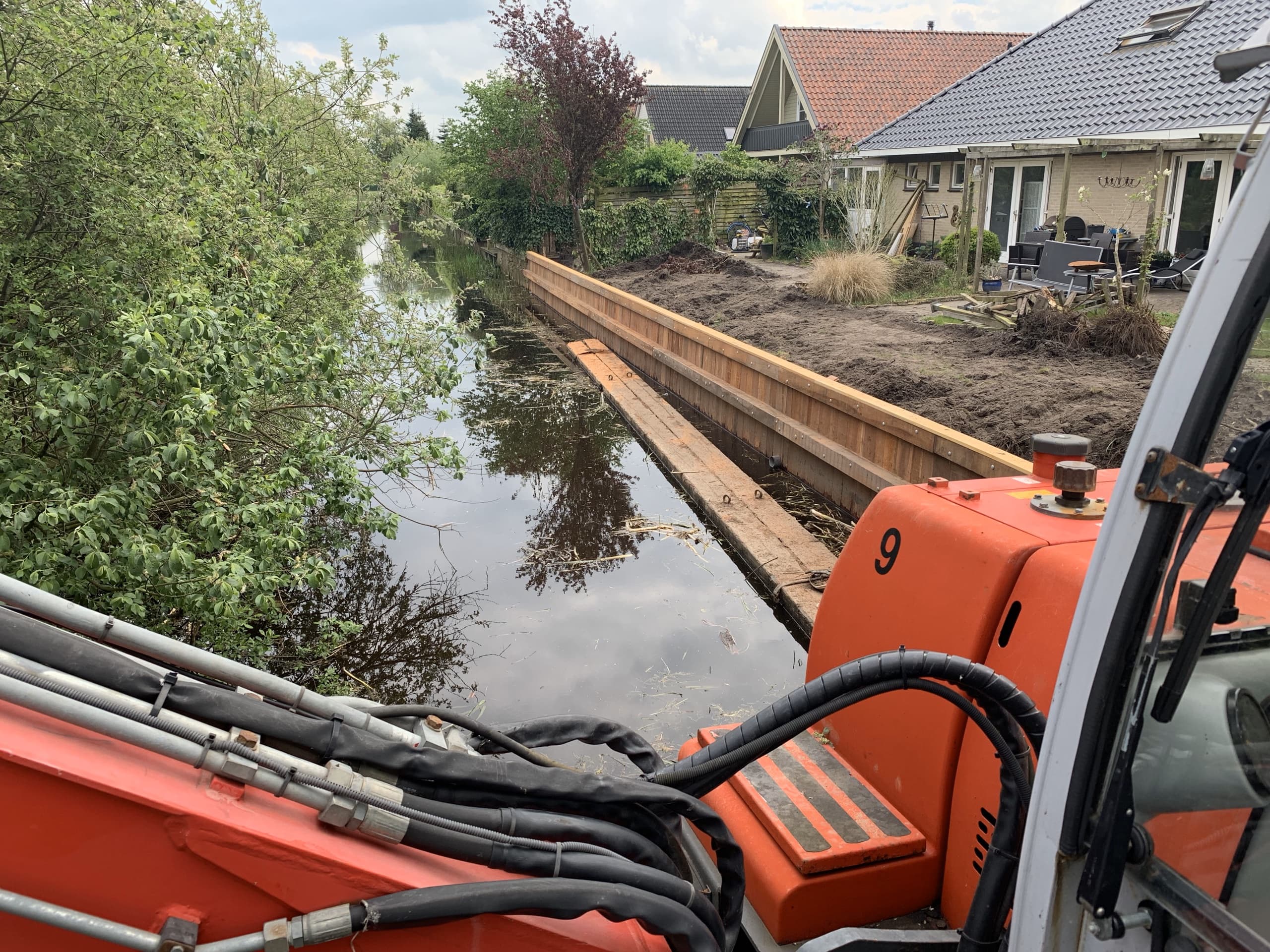 Zicht vanaf de rupskraan op de nieuwe houten wand, aangelegd tot tegen de achtertuinen van de woningen