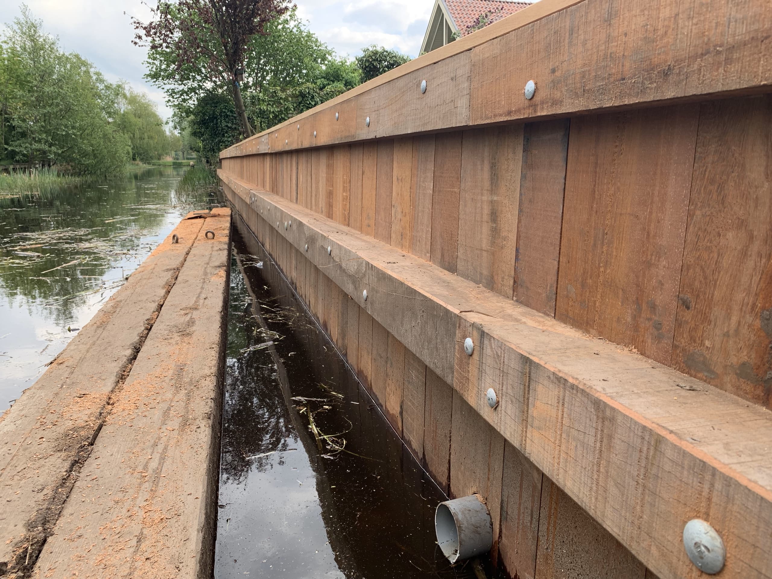 Detail van de afgewerkte walbeschoeiing: verticale planken tegen een liggende regel, vastgezet met rvs bouten