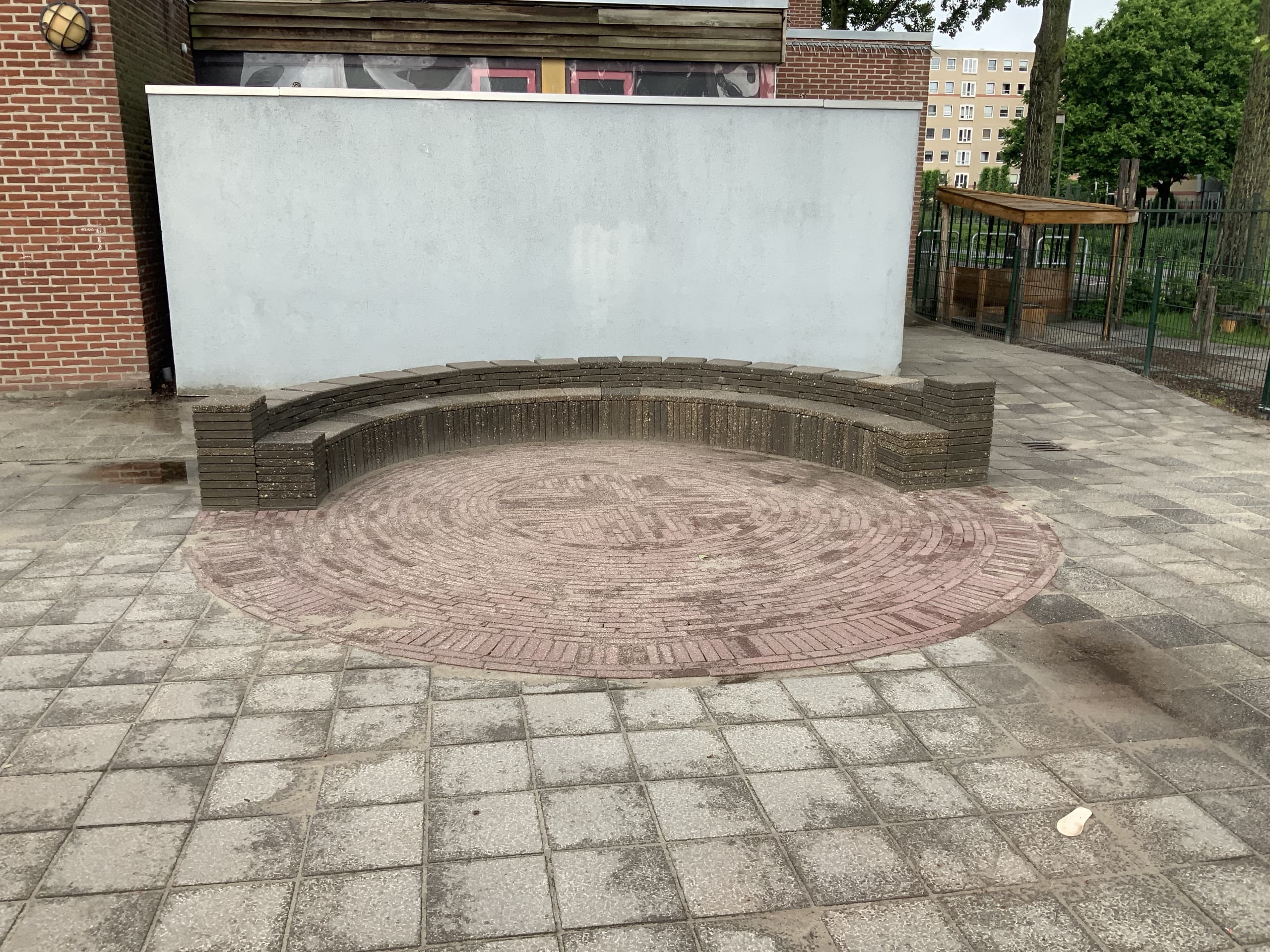 Het afgewerkte amfitheater tegen de gevel: een gemetselde zitrand rond een cirkelpatroon van sierbestrating