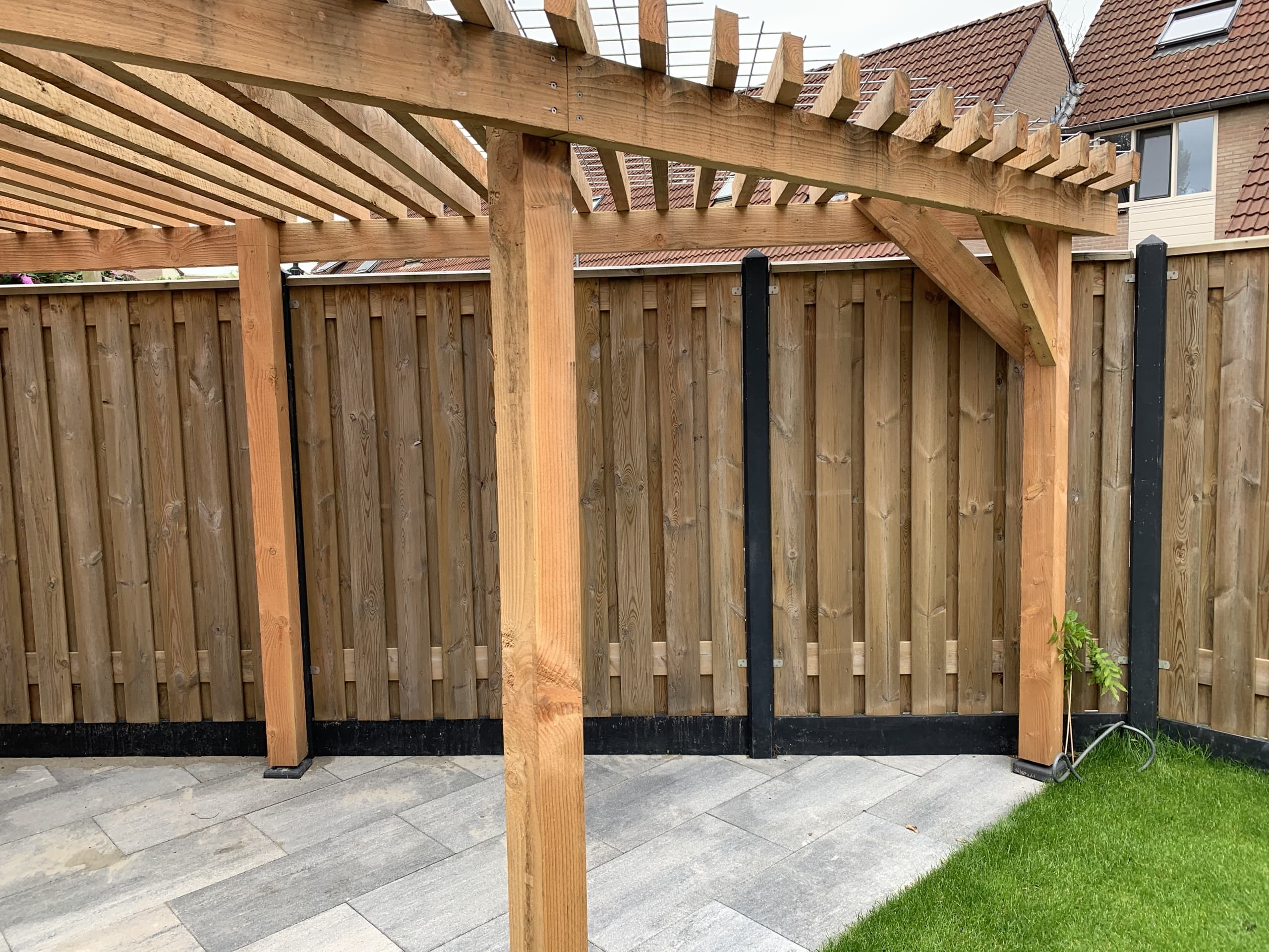 De houten pergola van dichtbij, met de balken tegen de schutting en het pad ervoor