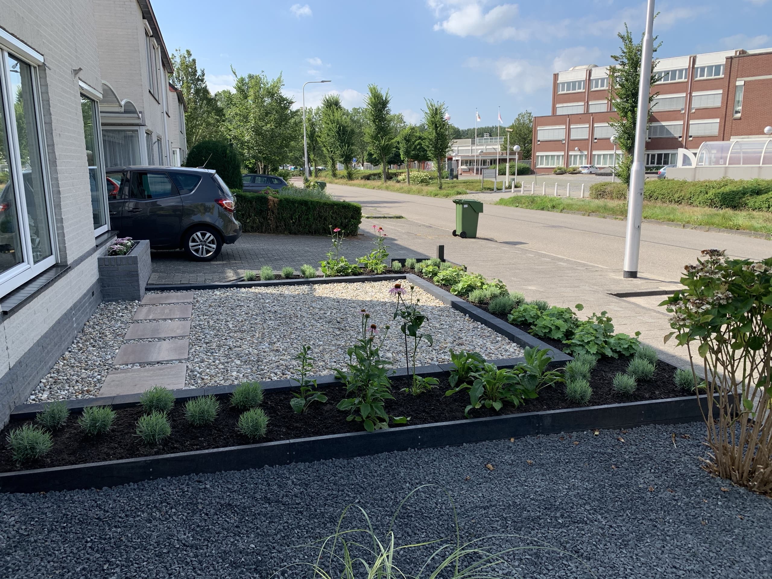 Het donkere grindvlak met border en stapstenen, gezien vanaf de gevel richting de oprit