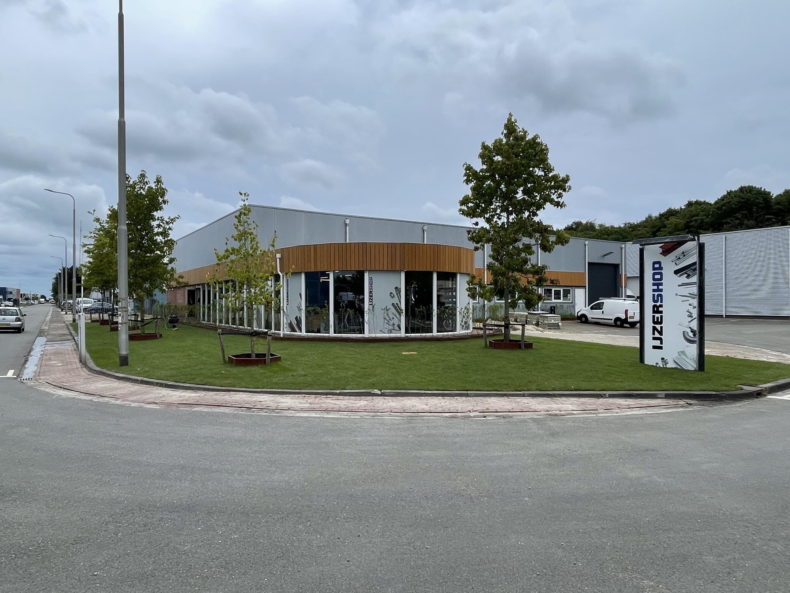 Het bedrijfspand van IJzershop op de rotonde, met een nieuw gazon en jonge bomen in cortenstalen boomkuipen rond de ronde pui