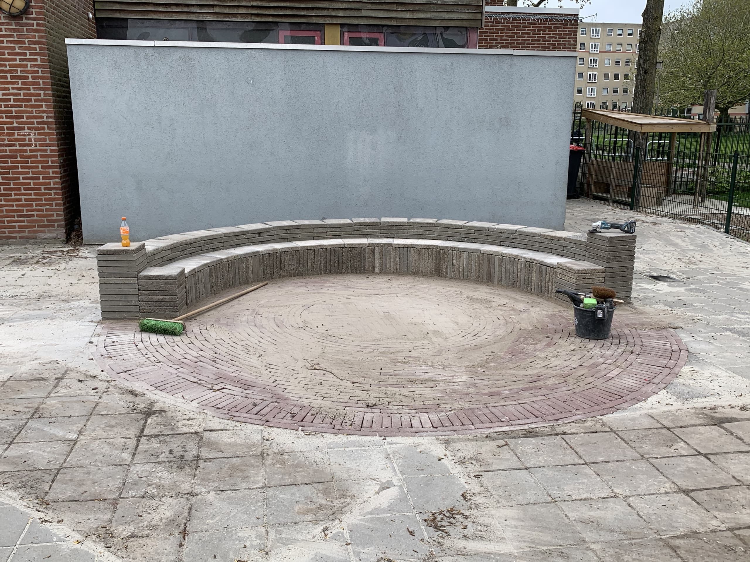 De gebogen zitrand van het amfitheater in aanbouw, met gereedschap op de nog onafgewerkte cirkel van sierbestrating