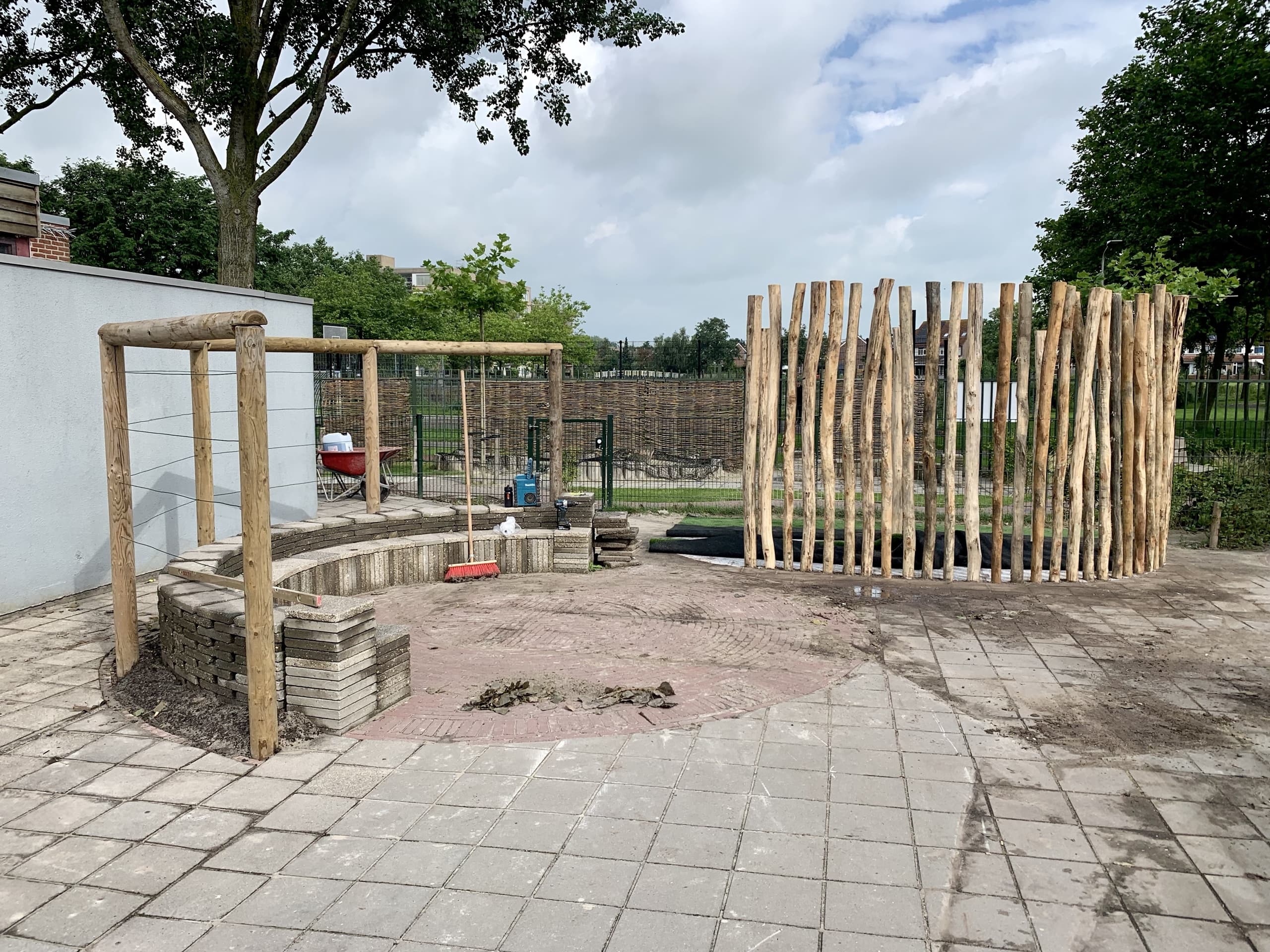 Het houten frame van het prieel in opbouw naast het net geplaatste vlechtwerkscherm van boomstammen