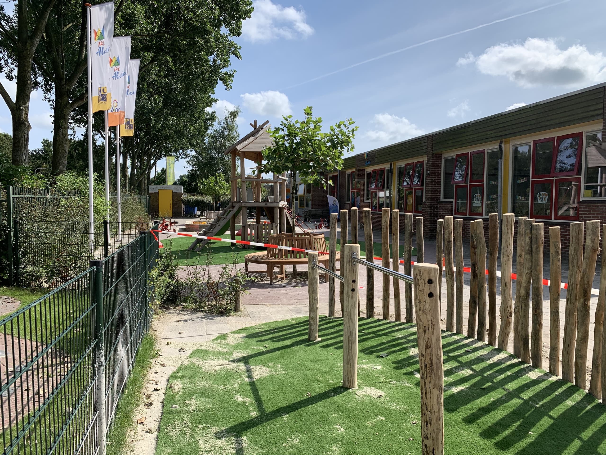 Het klimrek met evenwichtsbalken op het gazon, met de klimtoren en het schoolgebouw van IKC Alexia op de achtergrond