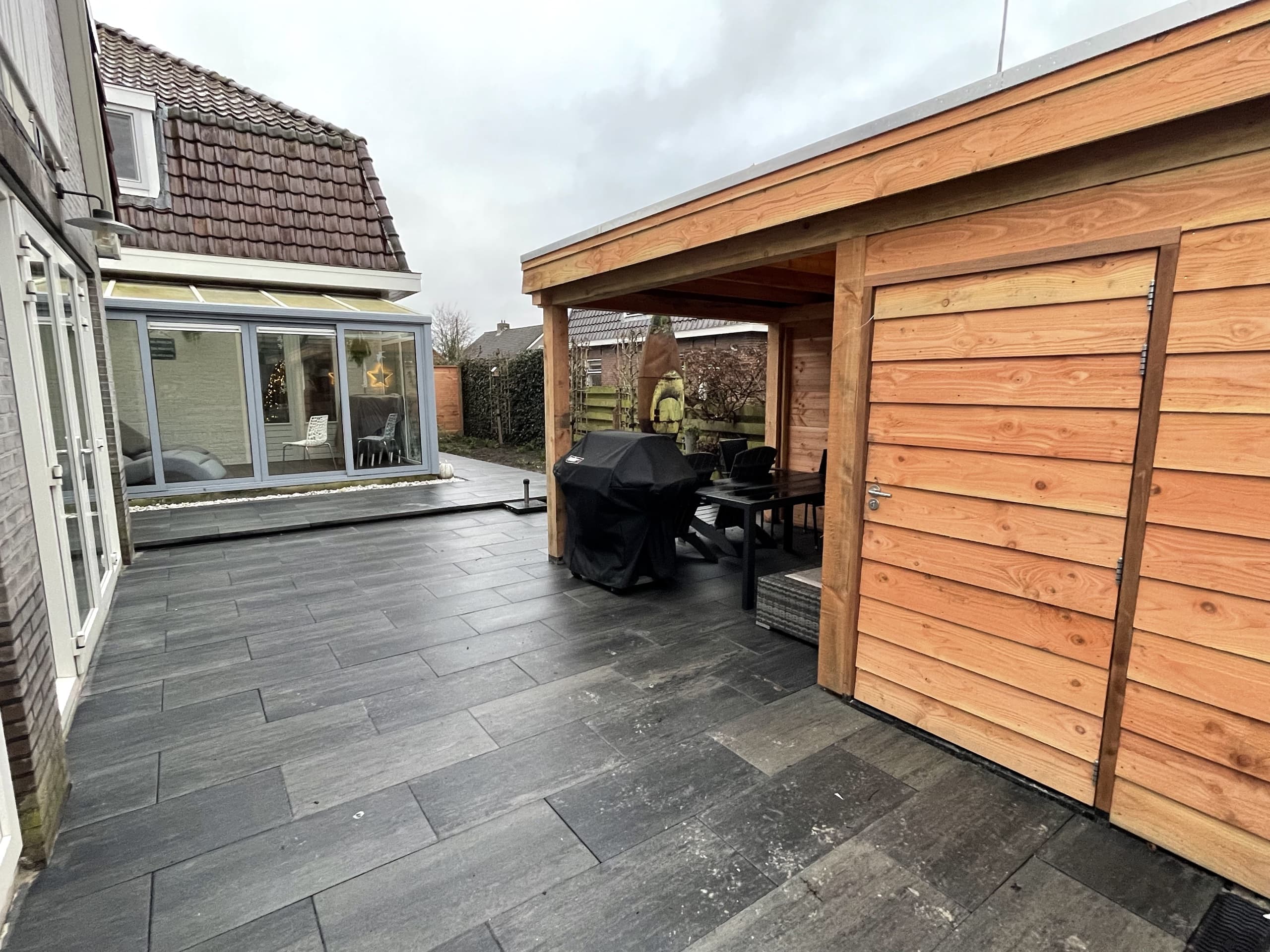 Tegelterras met houten overkapping en berging in een achtertuin in Warten