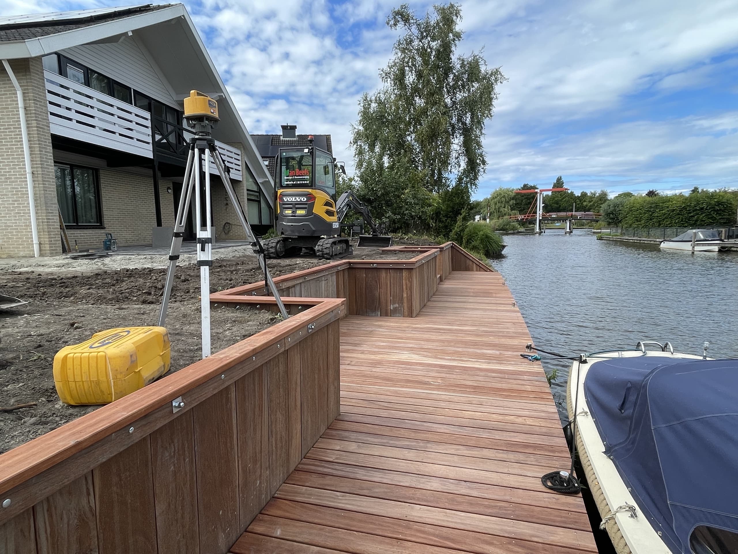De vlonder tijdens de bouw: waterpasapparatuur op statief, de minigraver van Van Beets en de ingebouwde plantenbakken in aanbouw