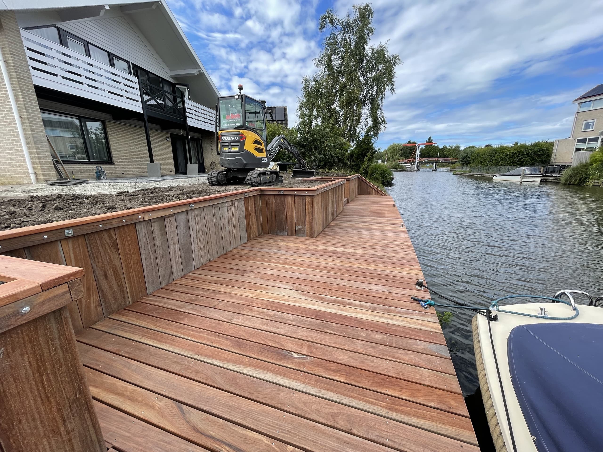 De vlonder in aanleg gezien richting het water, met de minigraver op de nog kale grond van de tuin