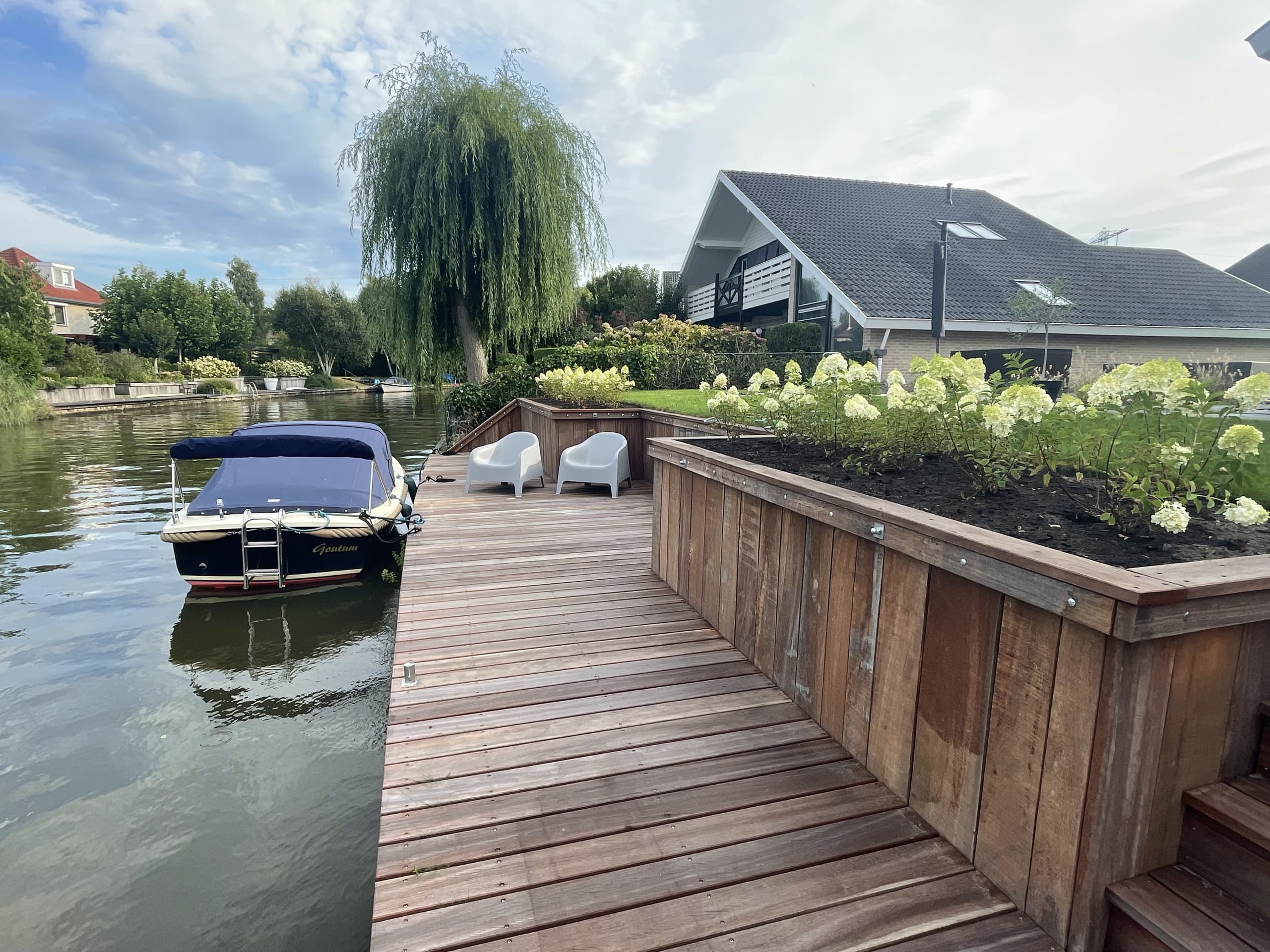 Hardhouten vlonder met plantenbakken vol hortensia's aan het water in Goutum, met een aangemeerde boot