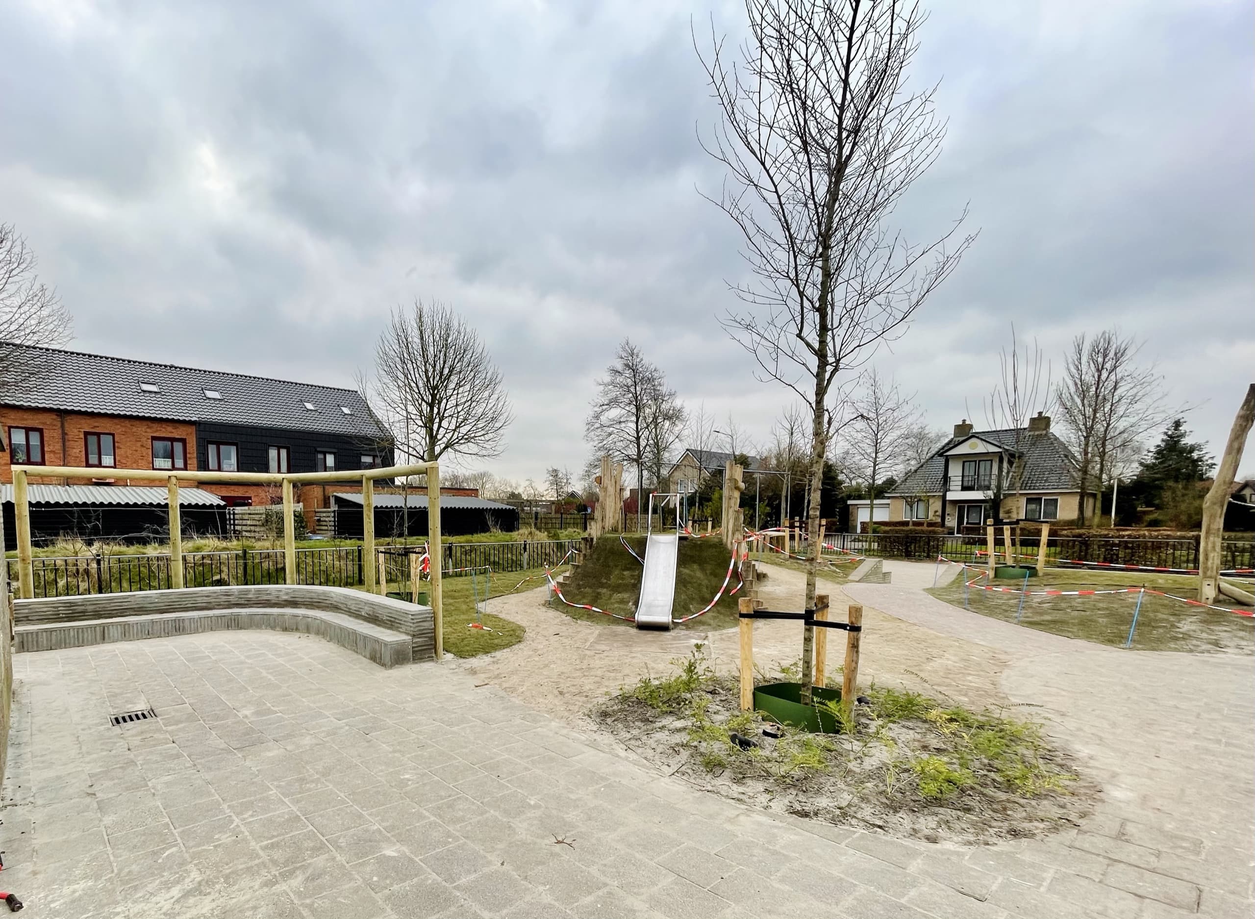 Overzicht van het schoolplein in Stiens met het amfitheater en de speelheuvel, en de nieuwbouwwijk op de achtergrond