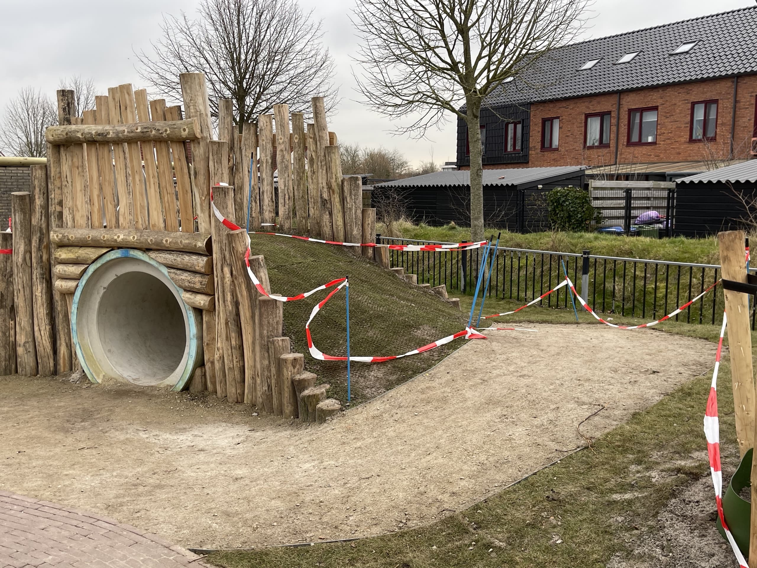 Zijaanzicht van de speelheuvel op het schoolplein in Stiens: de kruipbuis onder de houten palissade