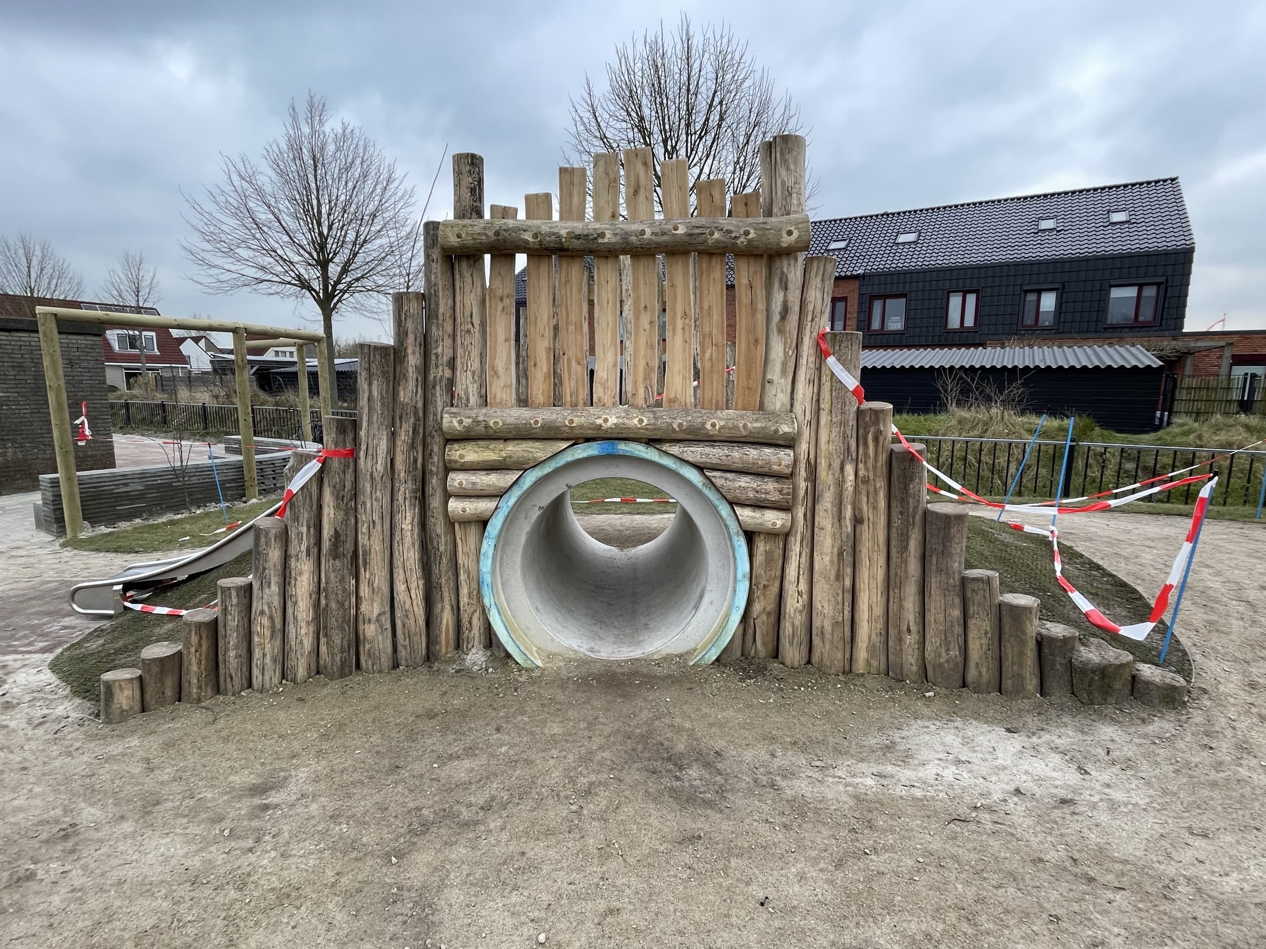 Houten palissade met kruipbuis en glijbaan in een speelheuvel op een schoolplein in Stiens