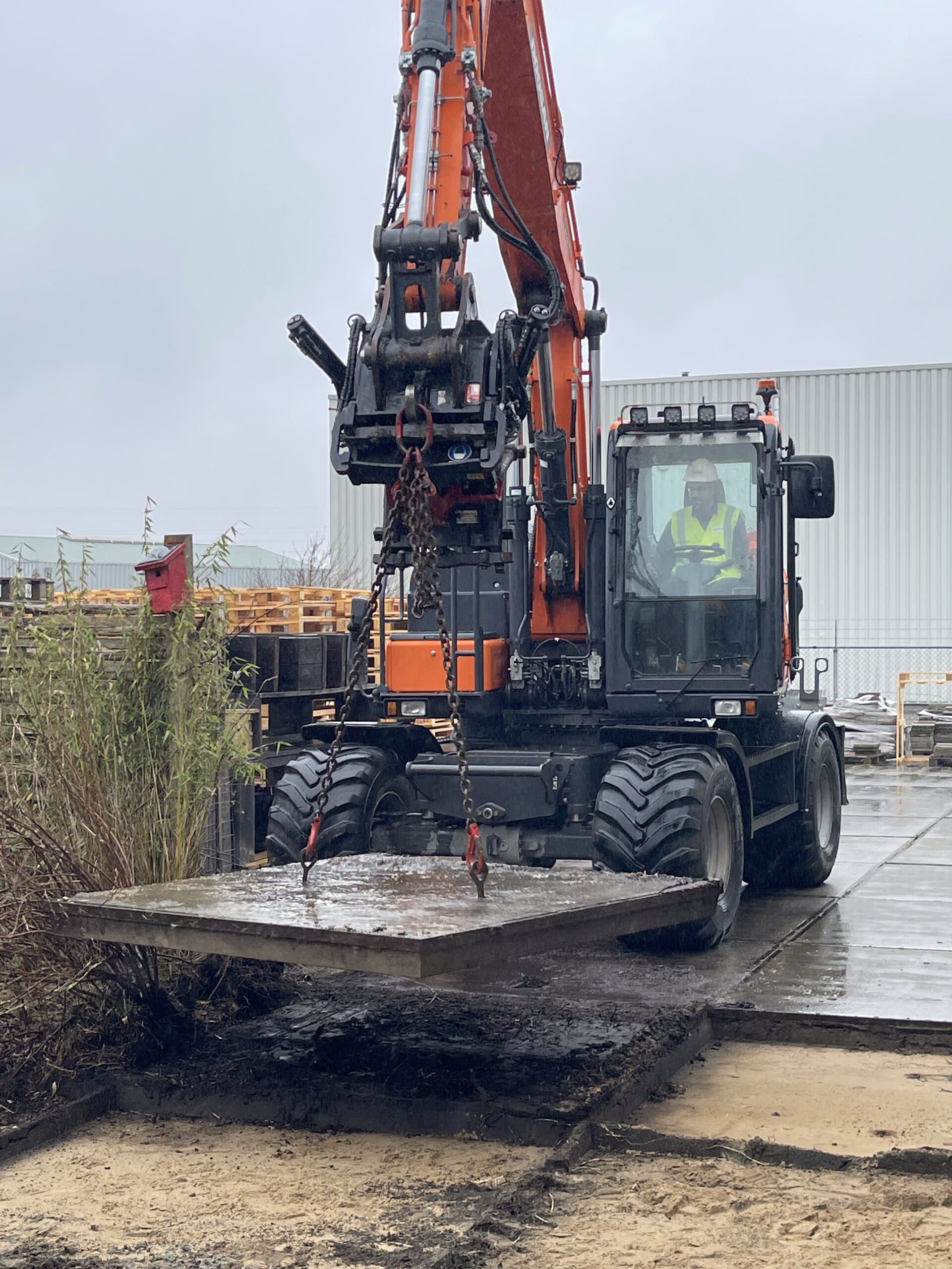 Betonplaat aan de haak van de graafmachine, met daaronder het vrijgekomen zand