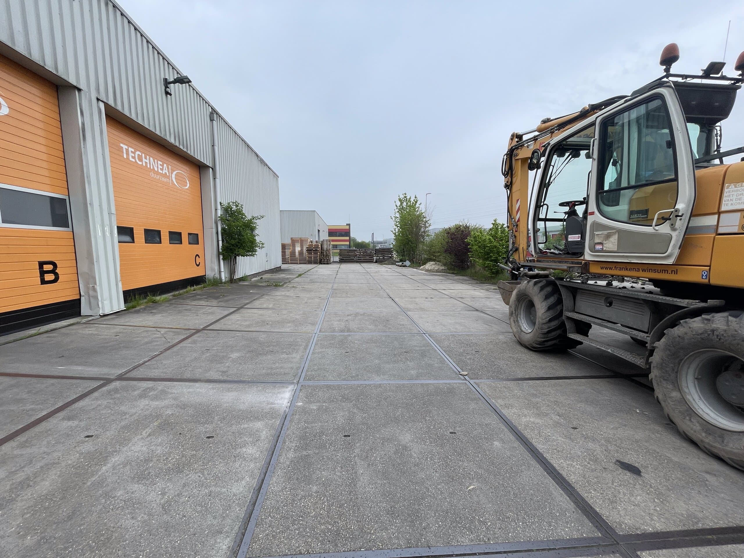 Het achterterrein van Technea voor de aanleg: betonplaten tot aan de oranje roldeuren van het bedrijfspand