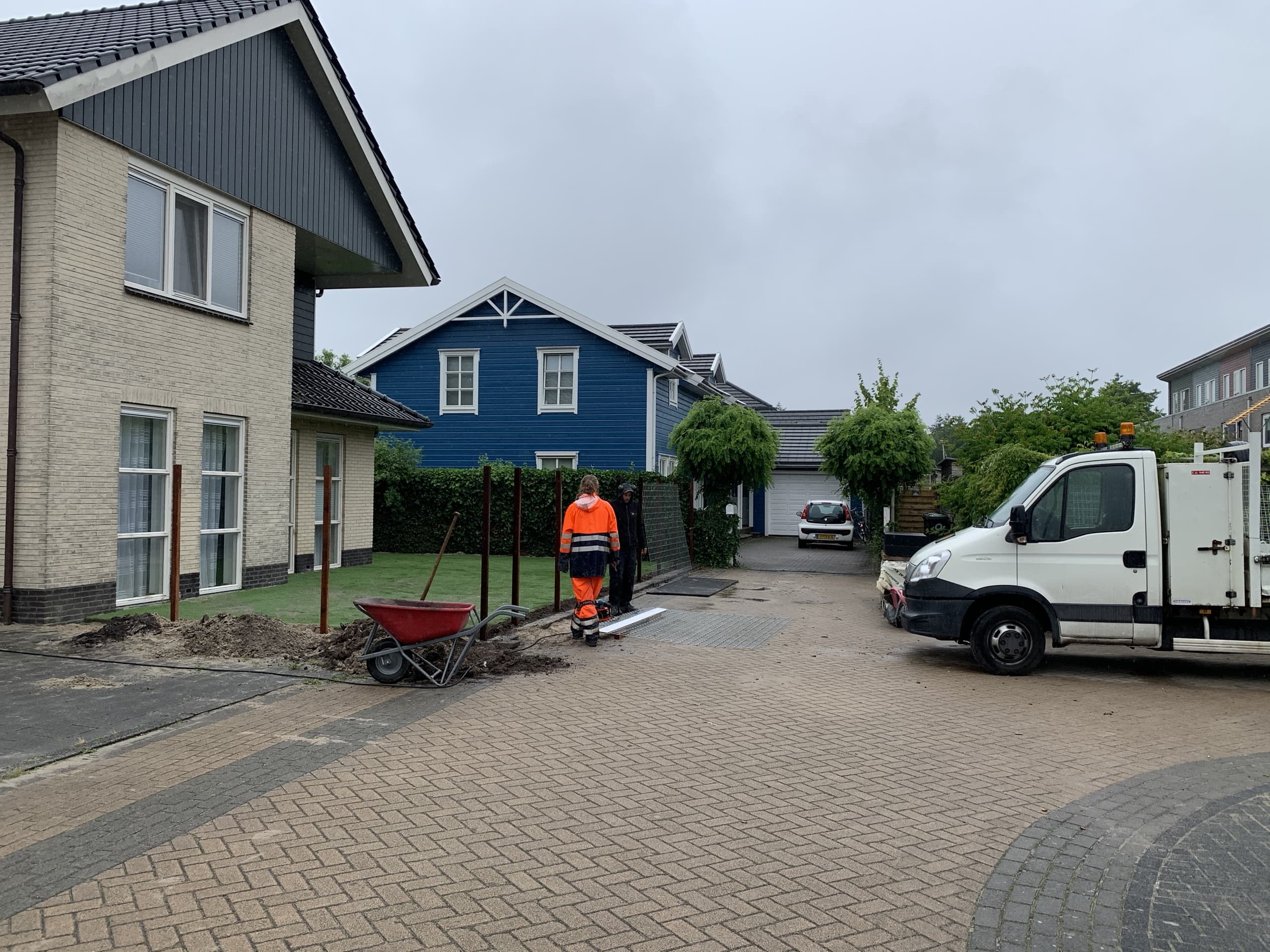 Aanvoer vanaf de straat in Drachten: rijplaten over de stoep, een kruiwagen met grond en de bus van Van Beets voor de deur