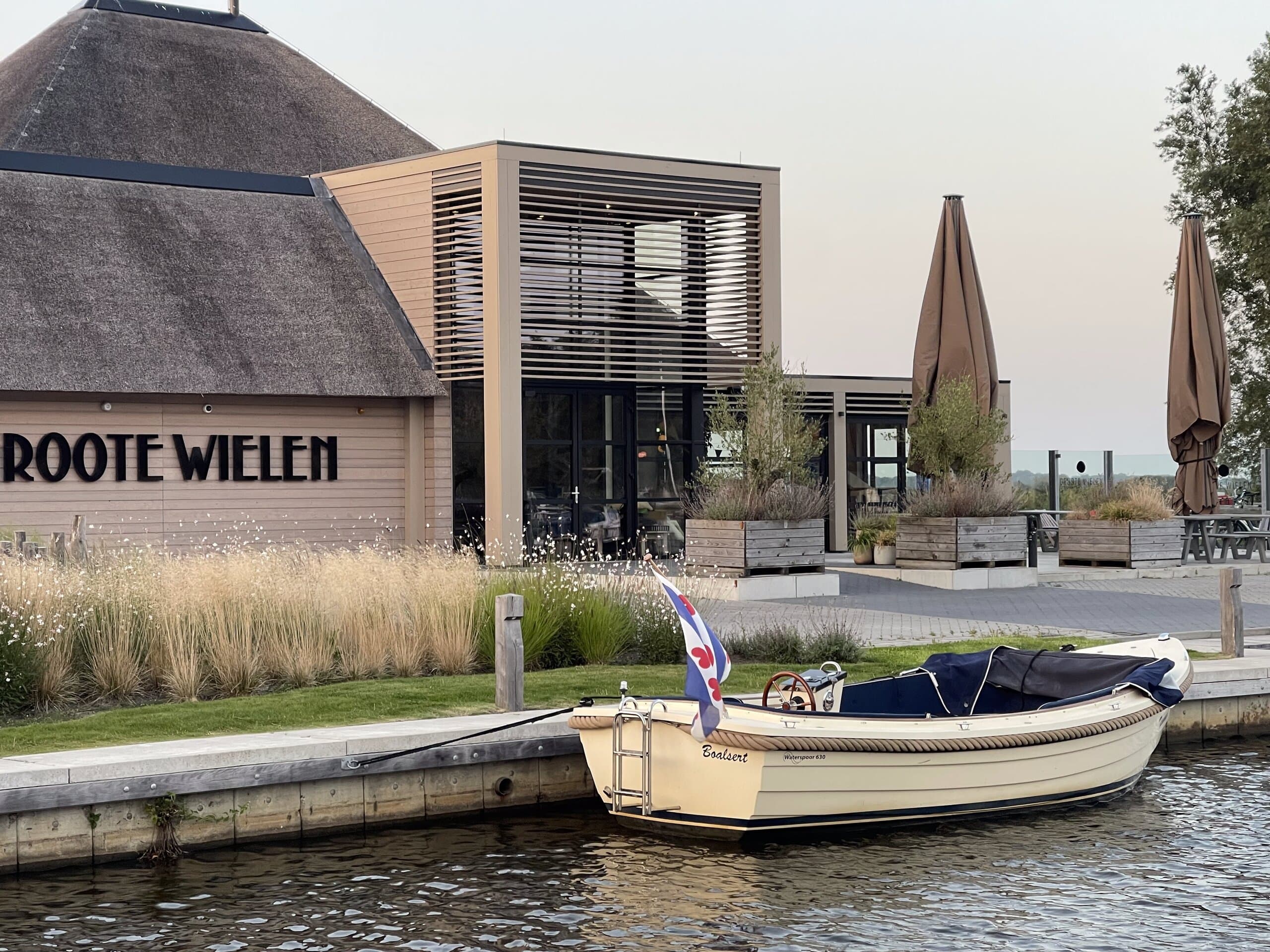 De siergrassen langs het water staan een jaar later in vol ornaat, met een sloep voor de kade
