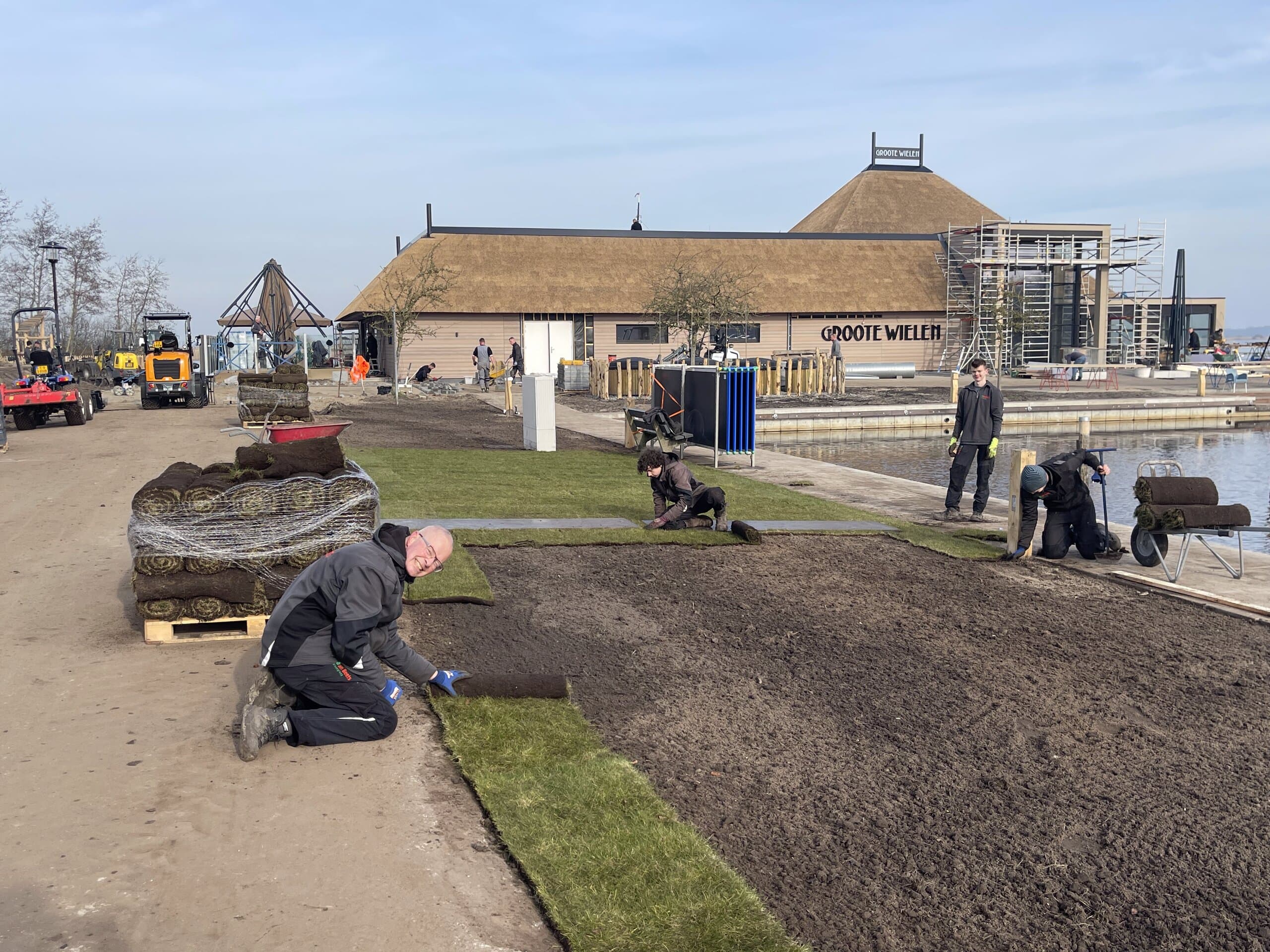 Hovenier van Van Beets rolt graszoden uit bij de aanleg van het terrein aan de Groote Wielen, met collega's verderop aan het werk