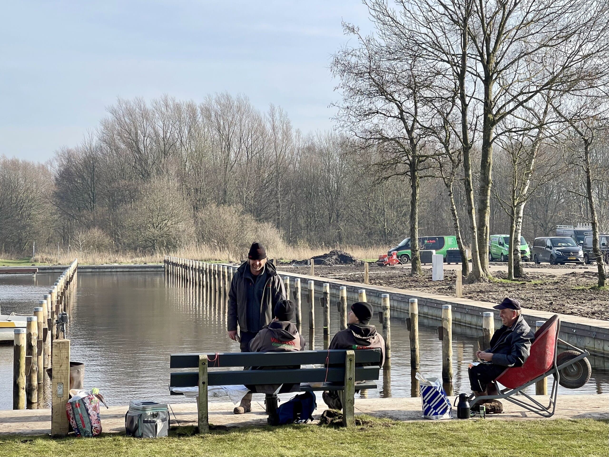 Het team pauzeert op een bank aan het water, naast de pas geplaatste steigerpalen