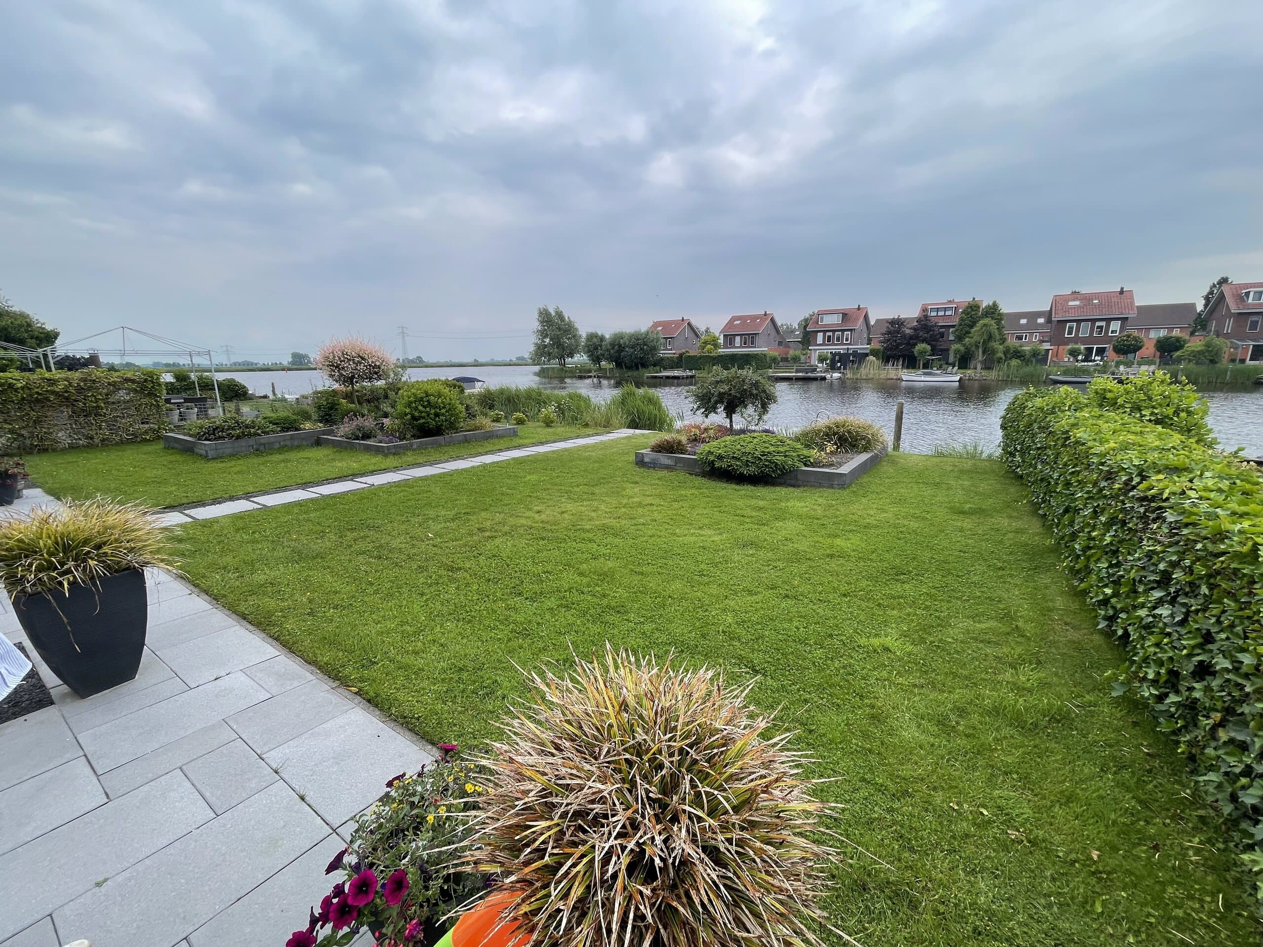 Ruim gazon met stapstenenpad tussen de verhoogde borders, en uitzicht over het water naar de overkant