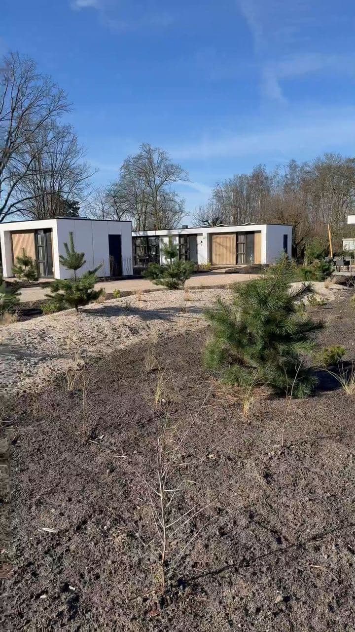 Groot groenonderhoud op een vakantiepark van MarinaPark in Bloemendaal: paden en plantvakken tussen de vakantiewoningen, de bus van Van Beets op het terrein, en vakken met jonge dennen en grassen
